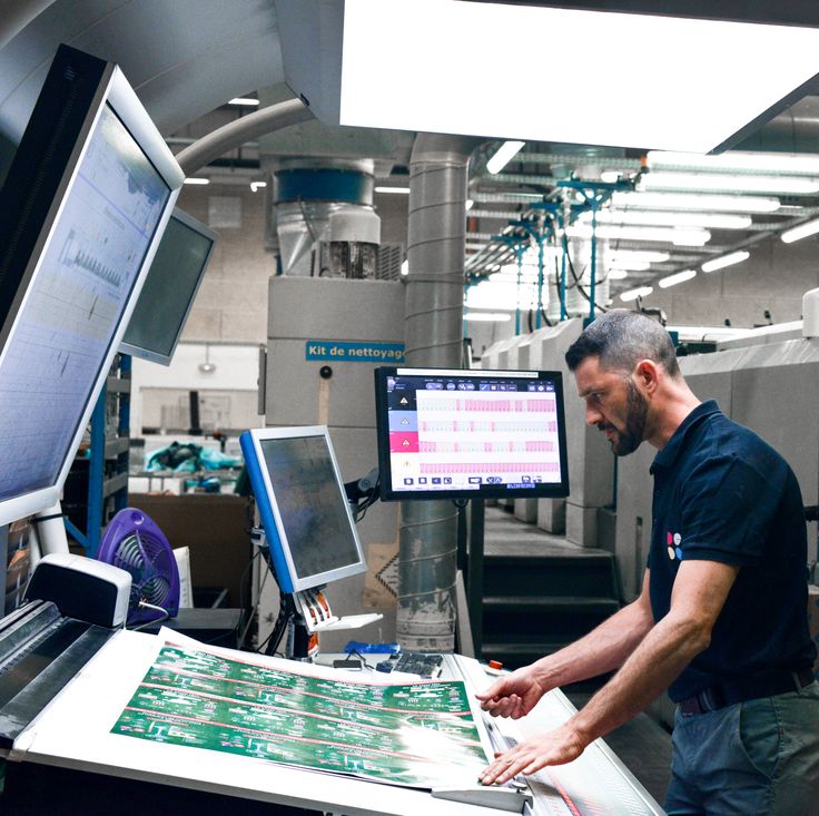 A press operator checking colour on a printed sheet at an inspection console.